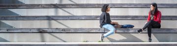 two students sitting on wooden stops outside